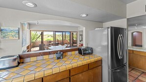 A kitchen with a large island, a refrigerator, and a view of the outdoors.