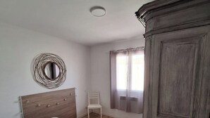 Ein Schlafzimmer mit einem Bett, einem Holzschrank, einem Stuhl und einem runden Spiegel an der Wand.