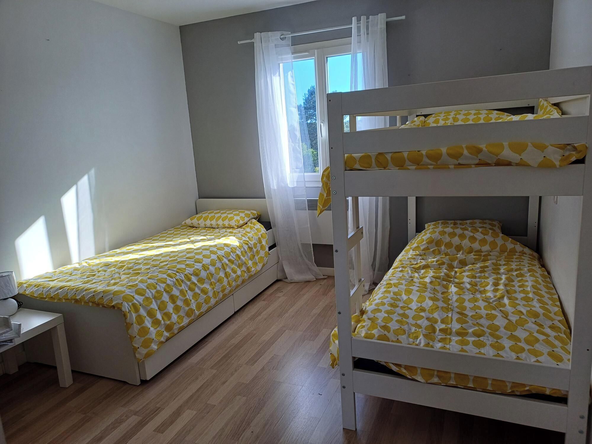 Een slaapkamer met twee enkele bedden, een klein nachtkastje en een raam met gordijnen.