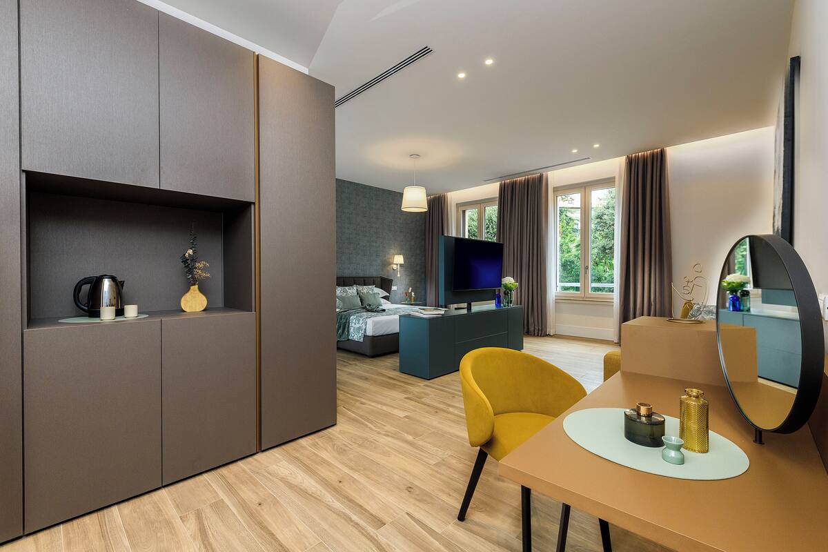 Ein modernes Hotelzimmer mit einer Couch, einem Esstisch, einem Fernseher und einem großen Fenster mit Vorhängen.