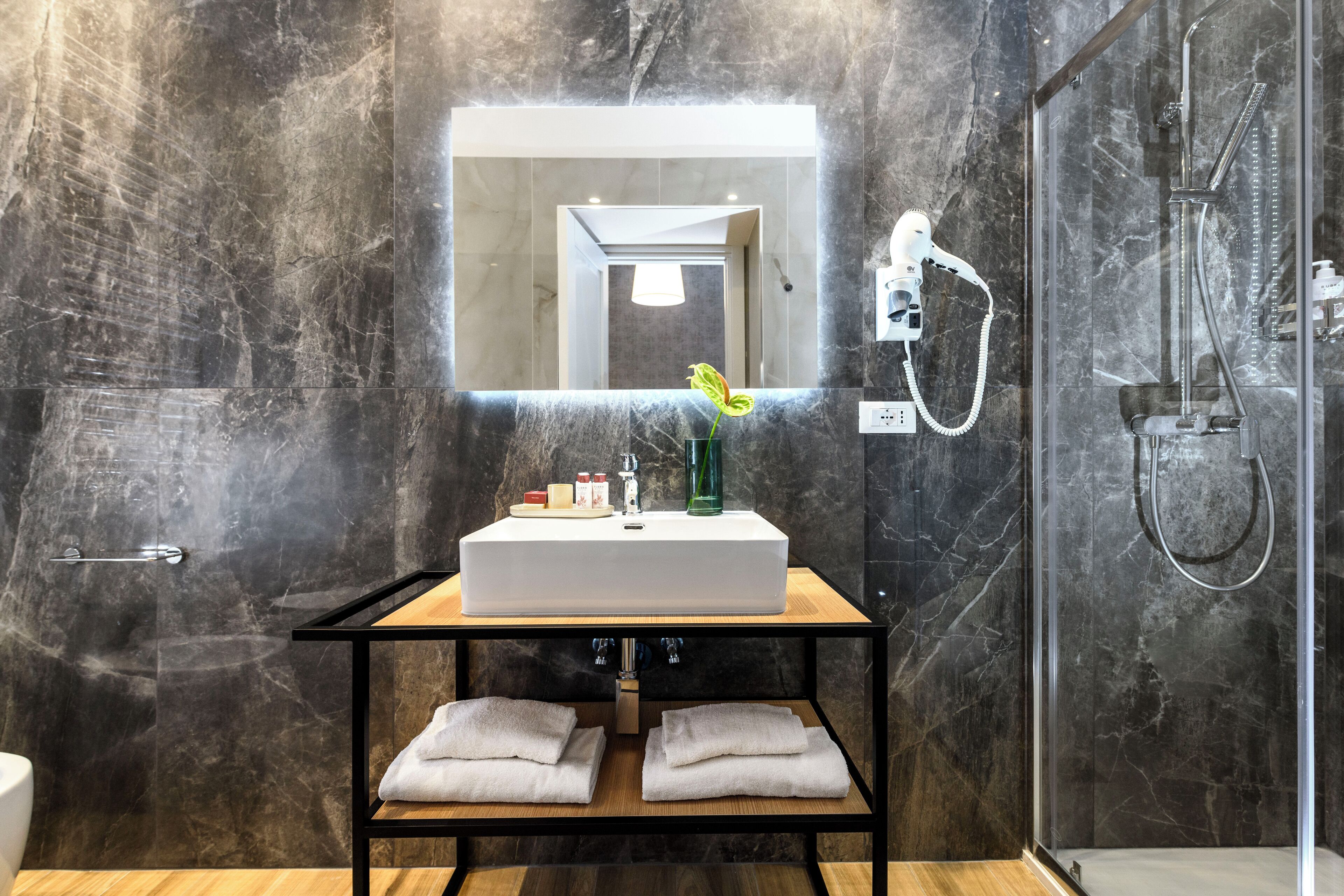 A modern bathroom with a marble wall, a white sink, a mirror, and a shower.