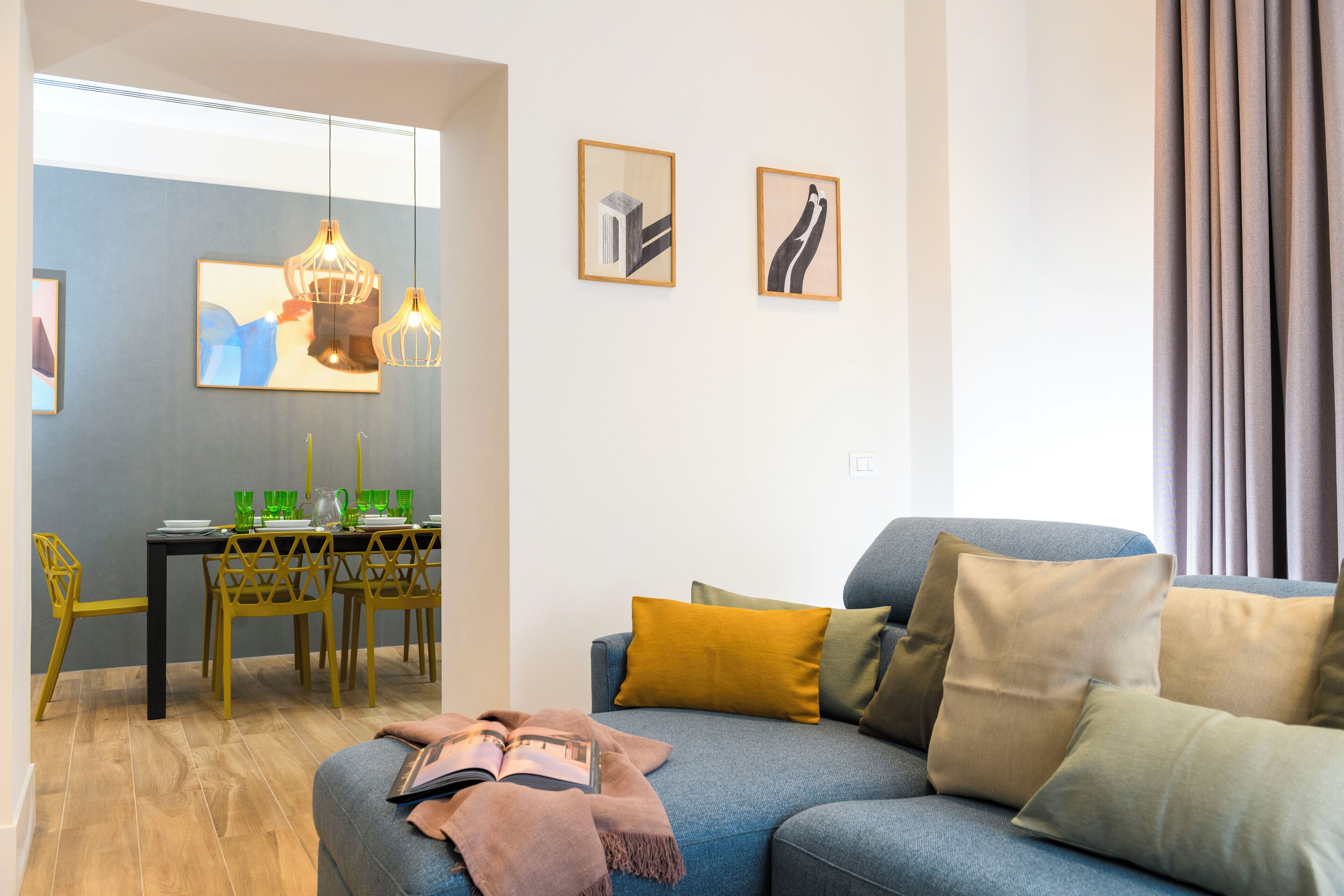 A modern living room with a sofa, cushions, a dining table with chairs, and artwork on the walls.