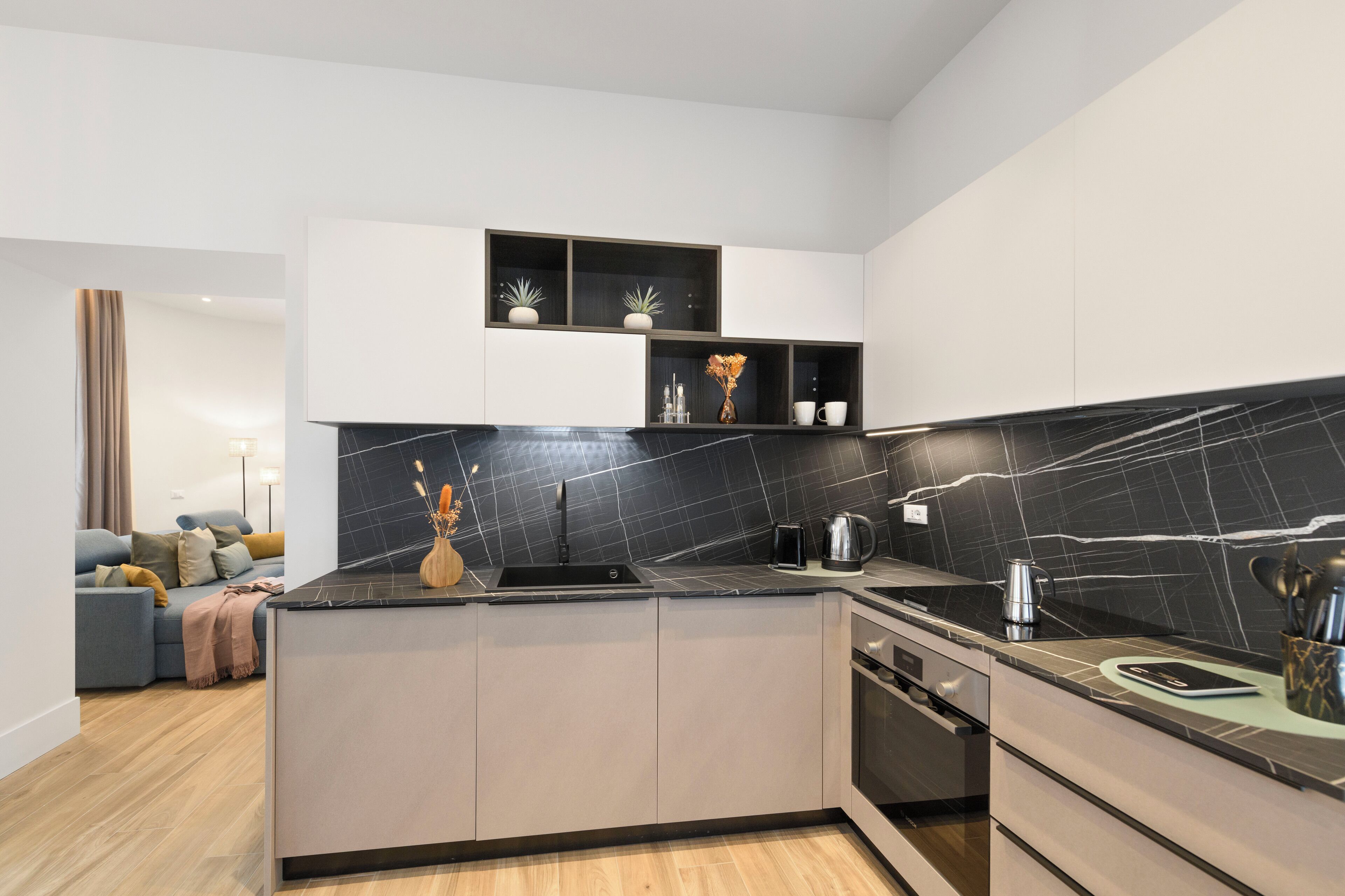 Una cocina moderna con salpicadero de mármol negro, armarios blancos y una isla integrada con fregadero.
