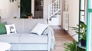 A modern living room with a sofa, a dining area, and a staircase leading to an upper floor.