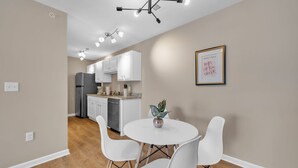 A modern kitchen with white cabinets, a stainless steel refrigerator, and a dining area with a round table and white chairs. - Stonecrest 620, 2Bd Apt I Free Parking I Pool (New Albany)