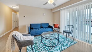 A modern living room with a blue sofa, two chairs, a glass coffee table, and a patterned rug. - Stonecrest 701, 2Bd Apt I Free Parking I Pool (New Albany)
