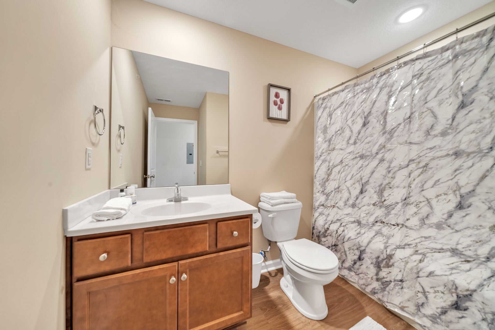 A bathroom with a marble shower wall, a white sink, and wooden cabinets.