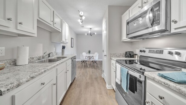 A modern kitchen with white cabinets, granite countertops, stainless steel appliances, and a dining area with a table and chairs. - Stonecrest 712, 2Bd Apt I Free Parking I Pool (New Albany)
