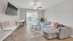 A modern living room with a grey sectional sofa, a round coffee table, a white bench, and a dining area with a table and chairs. - Stonecrest 712, 2Bd Apt I Free Parking I Pool (New Albany)