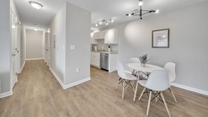 A modern kitchen with white cabinets, a dishwasher, and a dining area with a round table and white chairs. - Stonecrest 712, 2Bd Apt I Free Parking I Pool (New Albany)