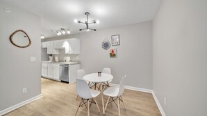 A modern kitchen with white cabinets, a dining area with a round table and four chairs, and a ceiling light fixture. - Stonecrest 713, 2Bd Apt I Free Parking I Pool (New Albany)