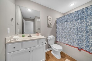 A bathroom with a white sink, mirror, and toilet. There is a blue patterned shower curtain and a white towel on the counter.