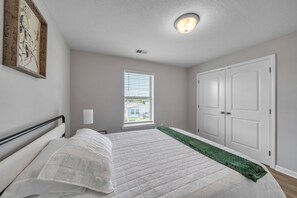 A bedroom with a bed, a window with blinds, a door, and a ceiling light.