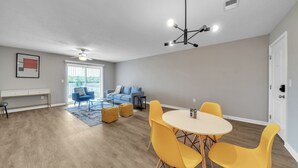 A spacious living room with a dining area, a blue sofa, a ceiling fan, and a modern chandelier. - Stonecrest 716, 2Bd Apt I Free Parking I Pool (New Albany)