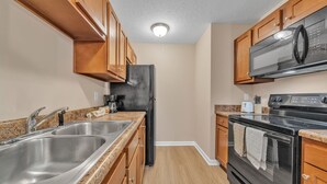 A kitchen with granite countertops, stainless steel appliances, wooden cabinets, and a black refrigerator. - Stonecrest 822, 2Bd Apt I Free Parking I Pool (New Albany)