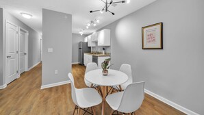 Une cuisine moderne avec des meubles blancs, un coin repas doté d’une table ronde et de chaises blanches, ainsi qu’un luminaire au plafond.