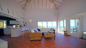A spacious living area with a kitchen, a dining area, and a large window overlooking the sea. - Villa Mahina, surfing and panoramic ocean views! (Le Moule)