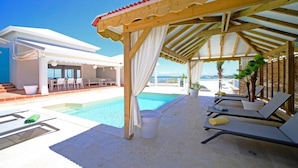 A poolside area with a covered seating area, lounge chairs, and a view of the sea. - Villa Mahina, surfing and panoramic ocean views! (Le Moule)