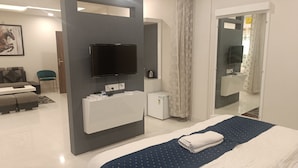 Ett modernt hotellrum med en stor säng, en platt-TV som är monterad på väggen, ett litet skrivbord med en spegel och ett separat badrum.