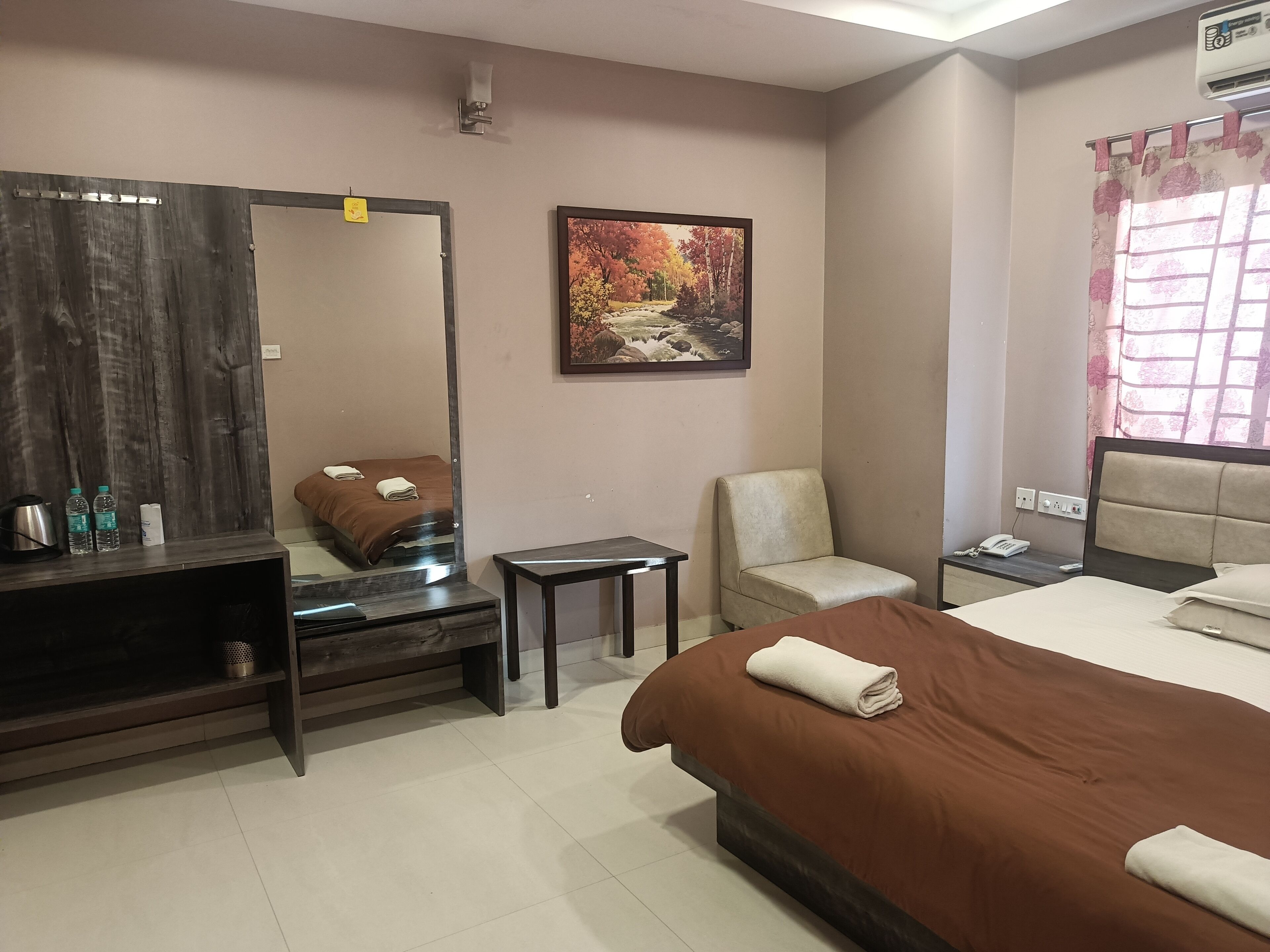 A hotel room with a bed, a chair, a small table, a mirror, and a painting on the wall.