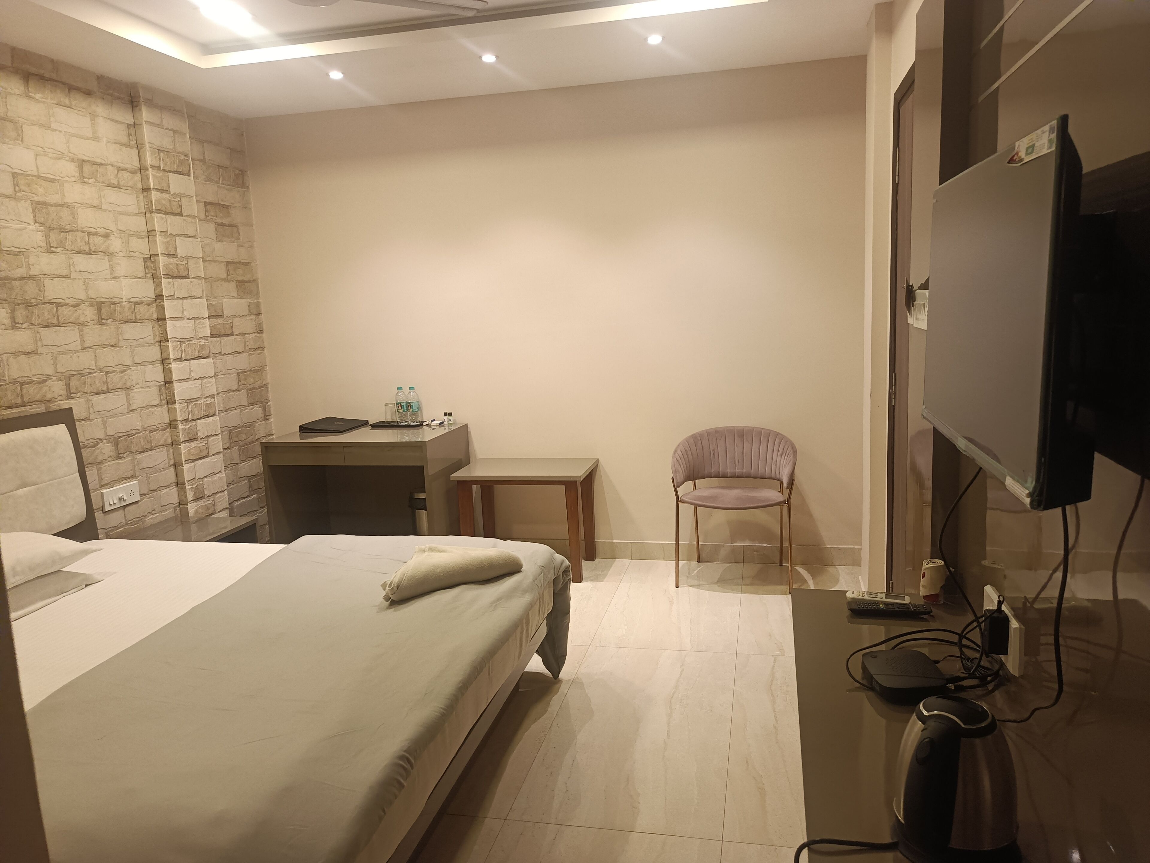 Habitación de hotel con cama, escritorio, silla, televisor y tetera.