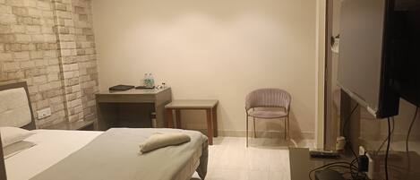 Habitación de hotel con cama, escritorio, silla, televisor y tetera.