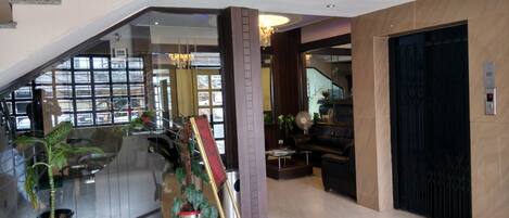 A modern hotel lobby with a staircase, a glass wall, a chandelier, and a black elevator.