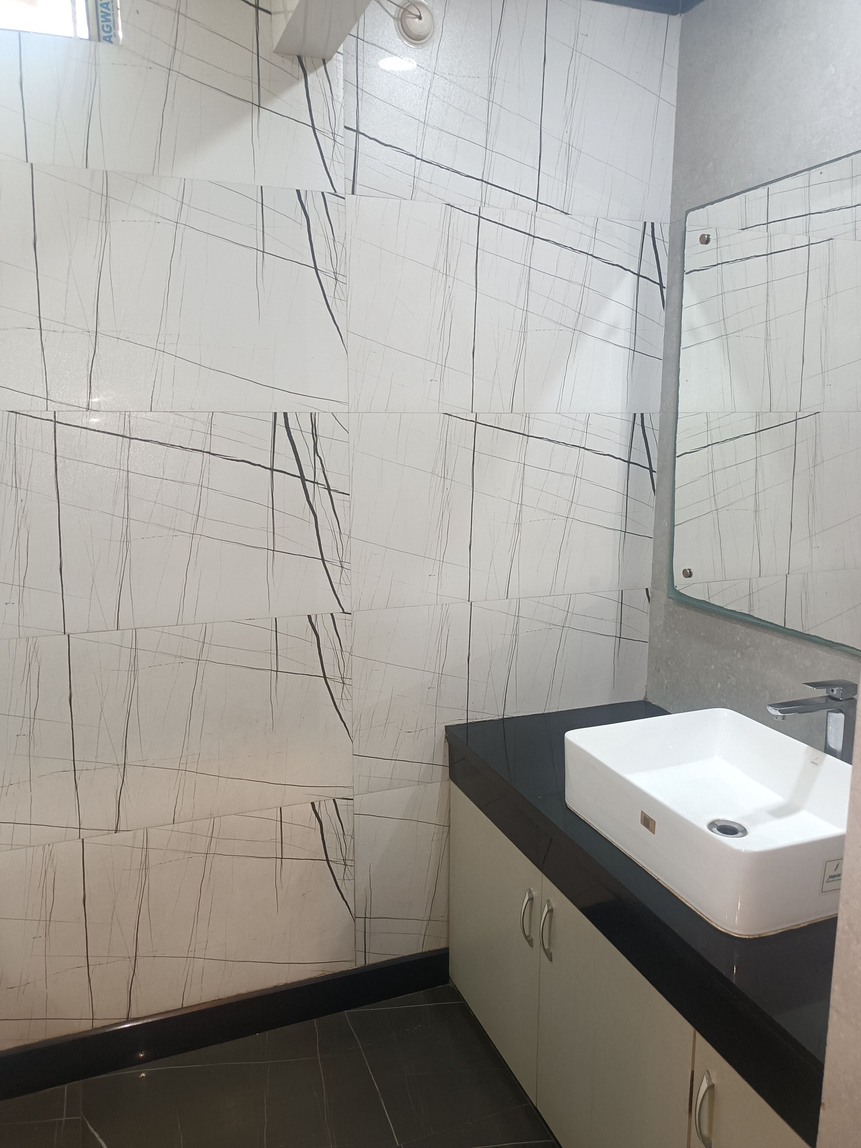 Une salle de bain avec des murs recouverts de carreaux blancs, un plan de toilette noir et un lavabo blanc.