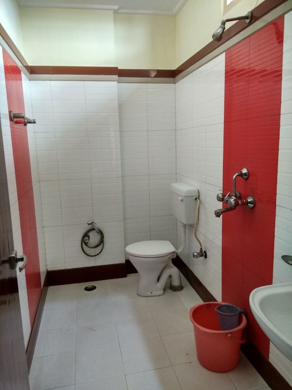 A small bathroom with a toilet, a red bucket, and a sink. - HOTEL RAJ PALACE by ROH (Dibrugarh)