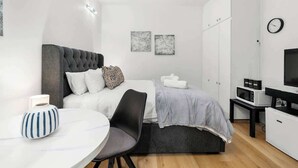 Een moderne slaapkamer met een bed, nachtkastje, stoel en een tv-meubel met een flatscreen televisie.