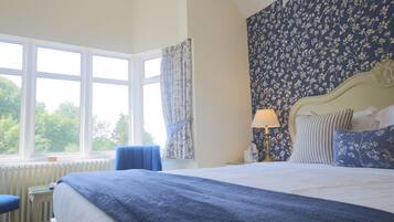 A bedroom with a large bed, a window with curtains, a radiator, and a nightstand with a lamp.