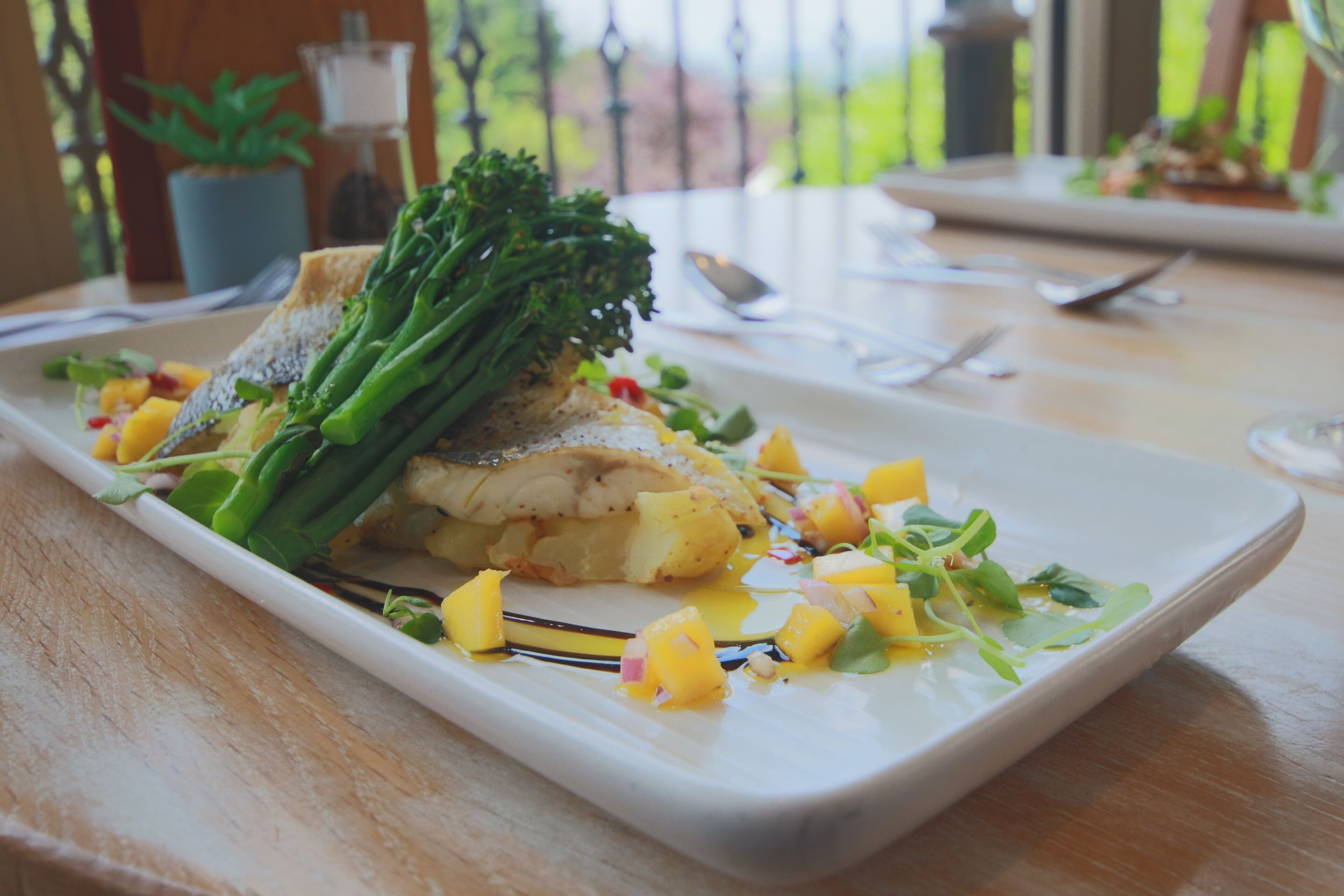 Un plato de comida con un filete de pescado, espárragos y mango sobre un plato blanco.