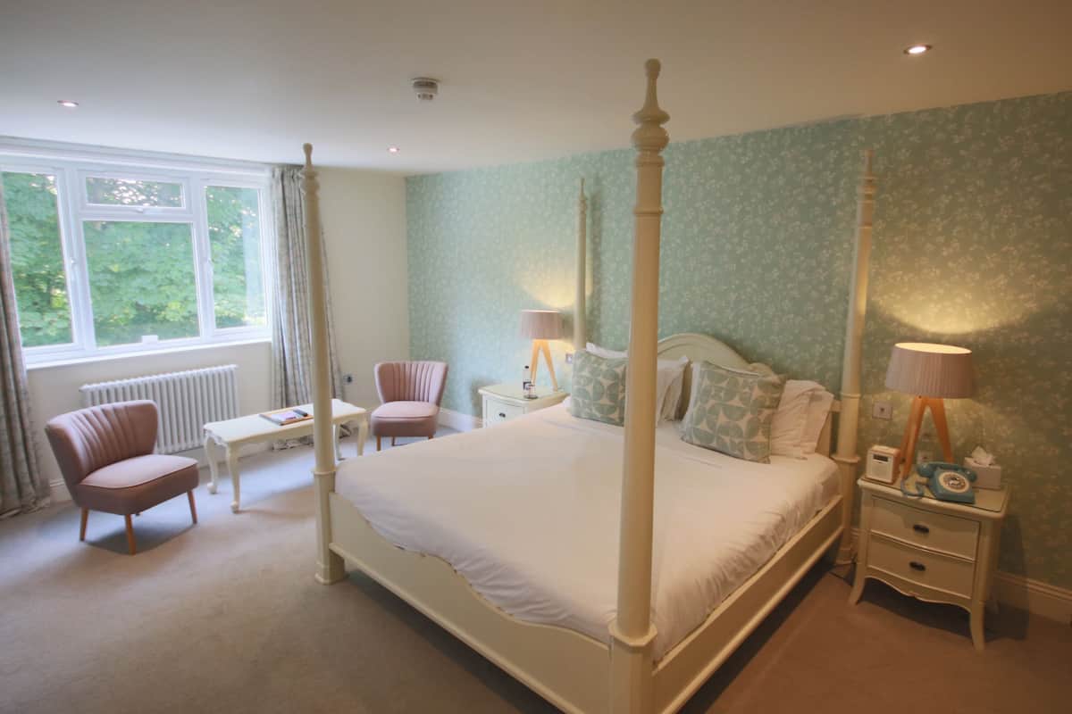 Un lit à baldaquin dans une chambre avec une fenêtre, une chaise, une table de chevet et une petite table de nuit.
