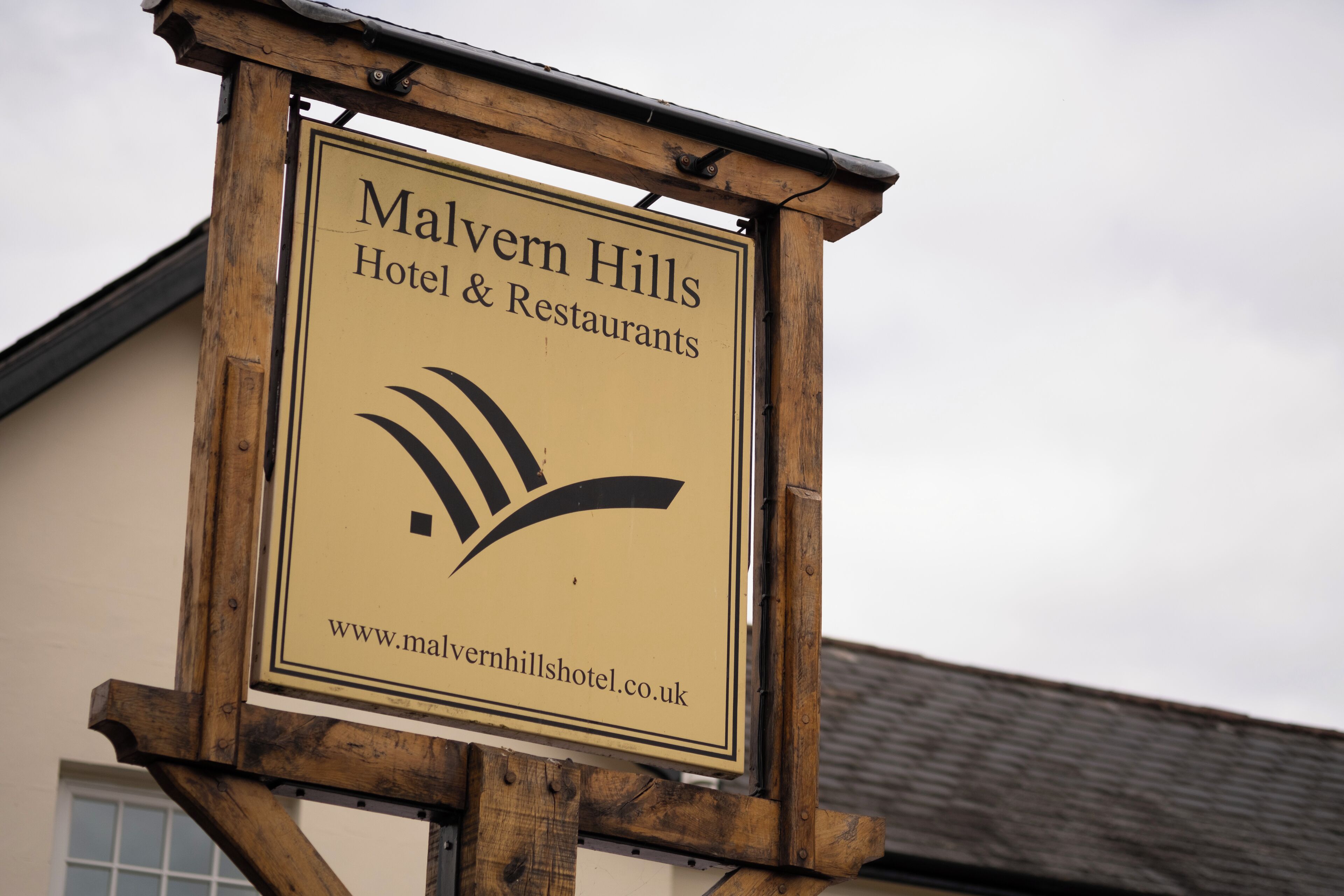 Een houten bordje voor Hotel & Restaurants Malvern Hills met een website-URL.
