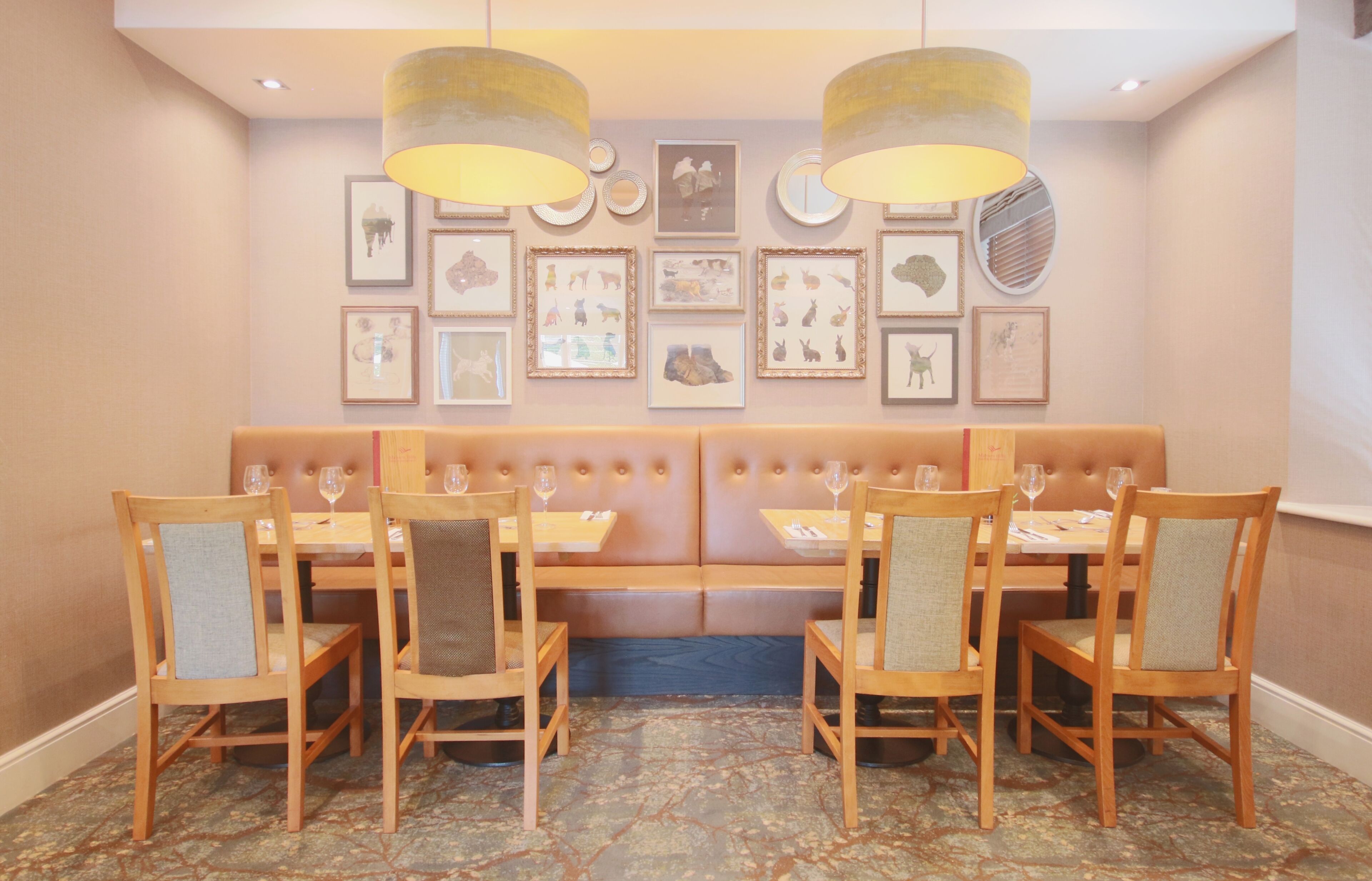 A dining area with a long bench, wooden chairs, and tables. There are framed pictures on the wall above the bench.