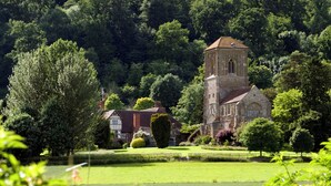 Une église historique, reconnaissable à son imposant clocher, entourée d’une végétation luxuriante et d’une pelouse bien entretenue.