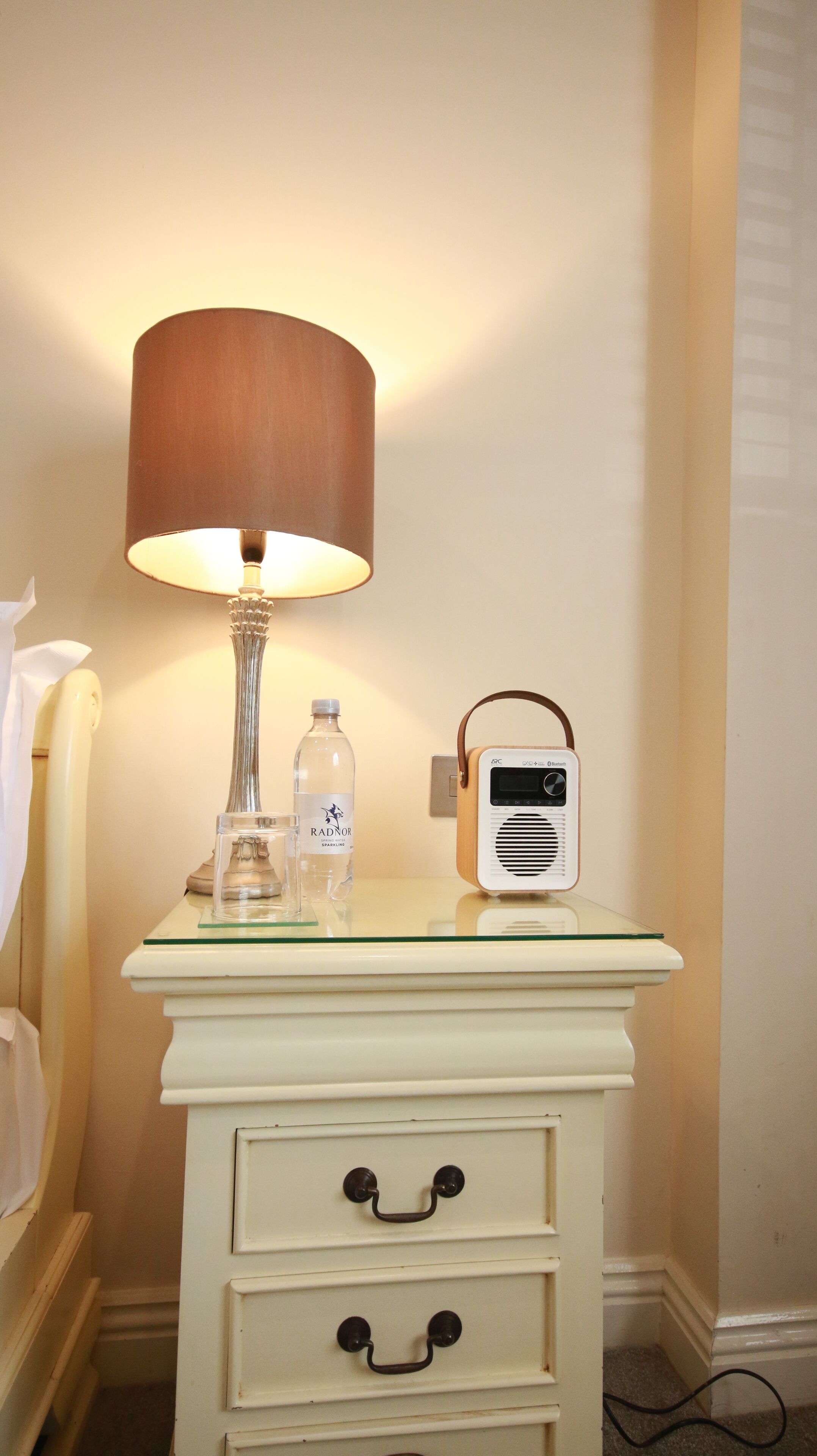 A bedside table with a lamp, a bottle of water, and a radio.