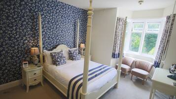 A four-poster bed with a white and blue striped bedspread, flanked by two bedside tables with lamps, a nightstand, and a window with curtains.