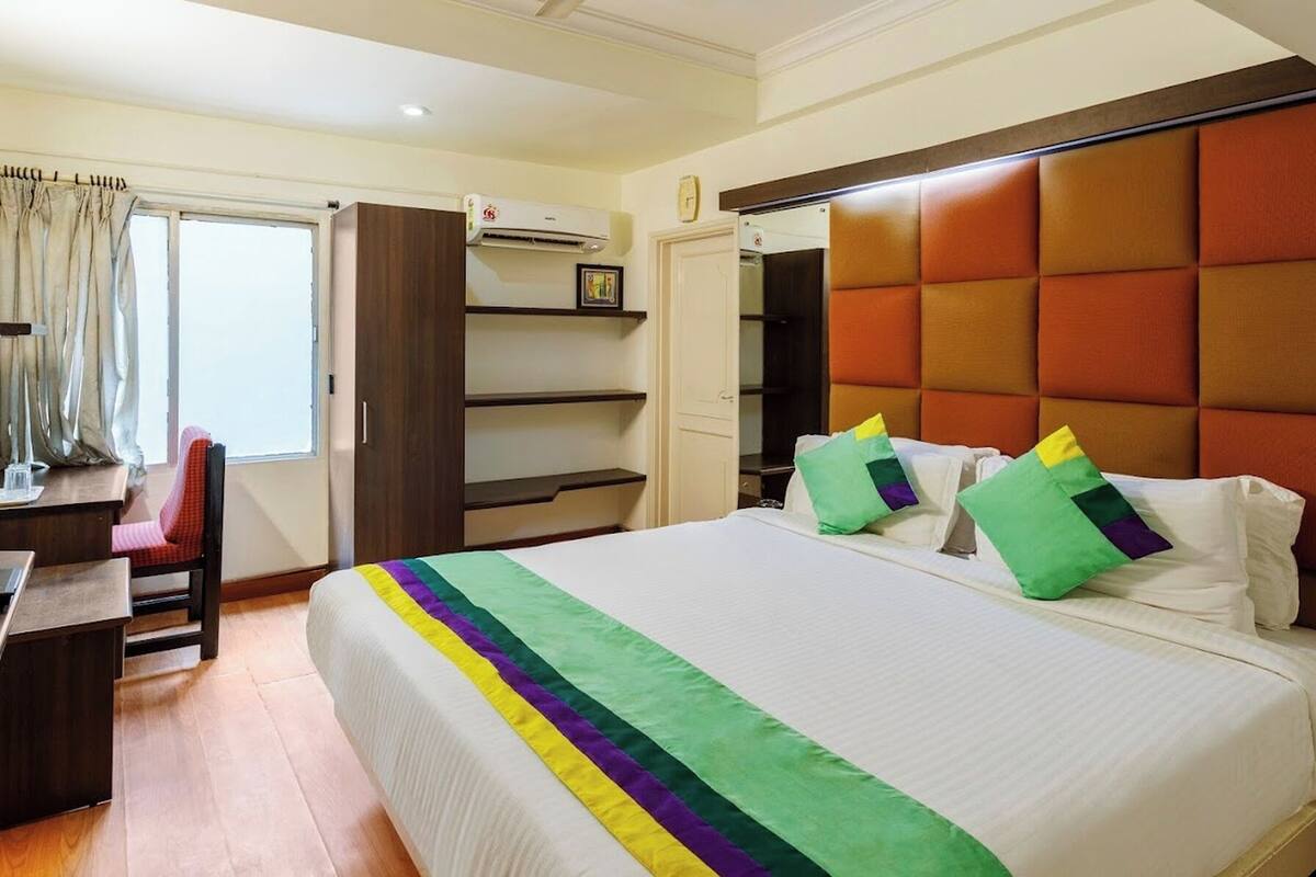 A hotel room with a bed, a desk, a chair, a wardrobe, and a bedside telephone.