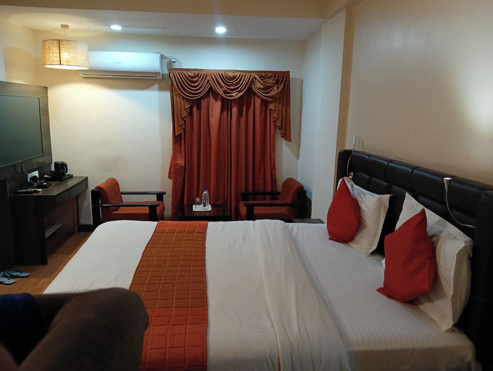 A hotel room with a bed, two chairs, a desk with a TV and coffee maker, and a window with curtains.