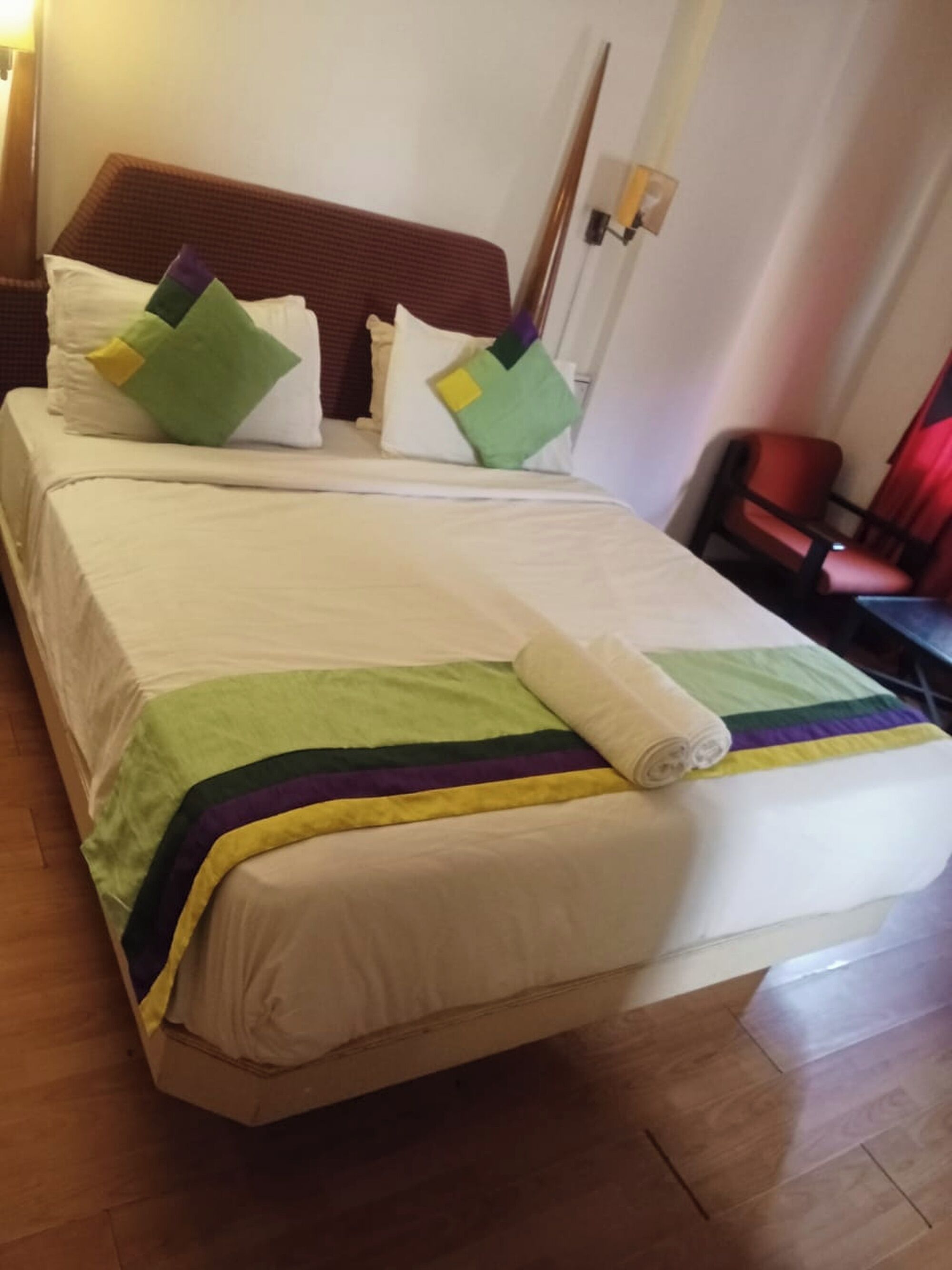 A neatly made bed with a striped blanket and a rolled towel, a wooden headboard, and a chair in the corner.