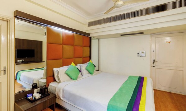 A hotel room with a bed, a TV mounted on the wall, a bedside table with a tray of amenities, and a door with a lock.