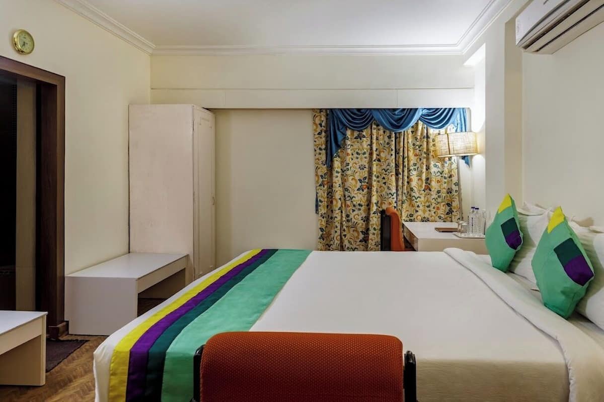 A hotel room with a bed, a desk, a chair, and a window with curtains.