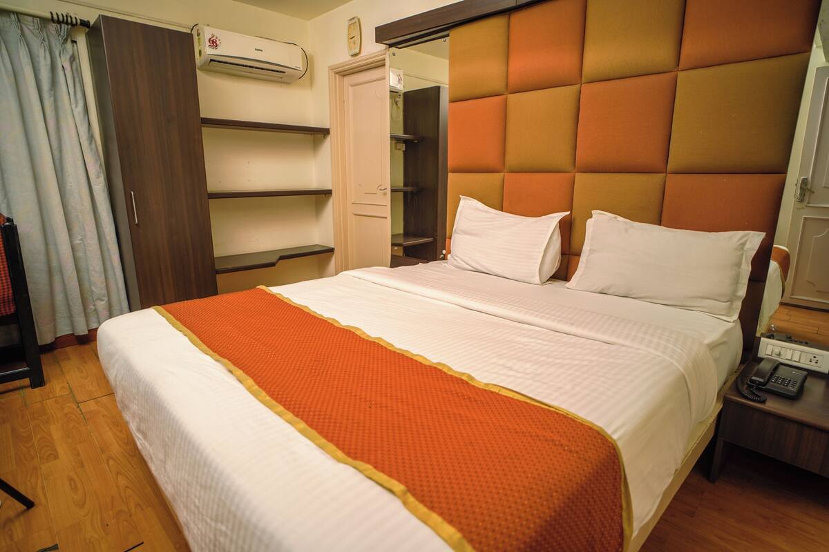 A hotel room with a large bed, a wardrobe, a mirror, and a bedside table with a phone.