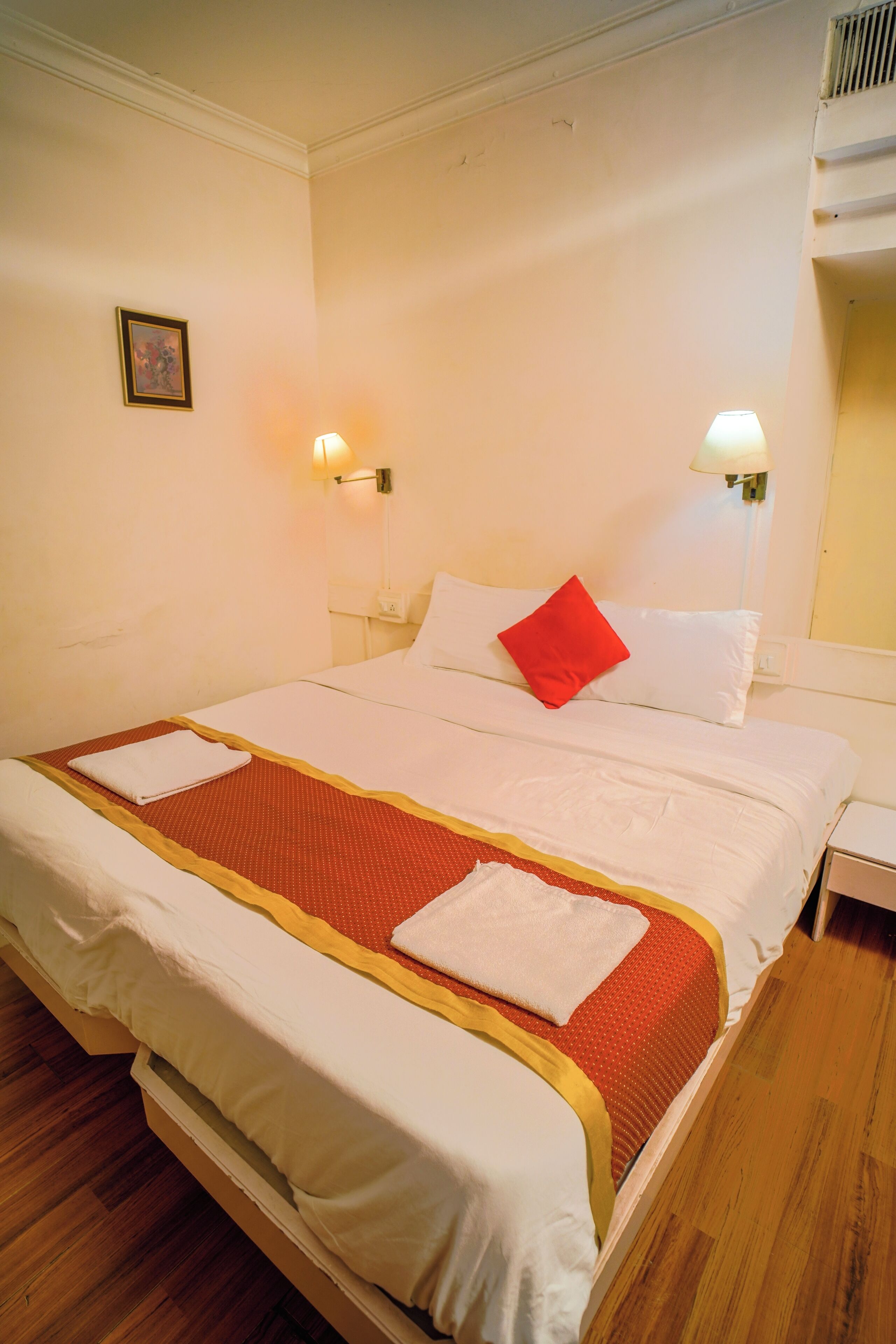 A hotel room with a neatly made bed, two bedside lamps, and a framed picture on the wall.