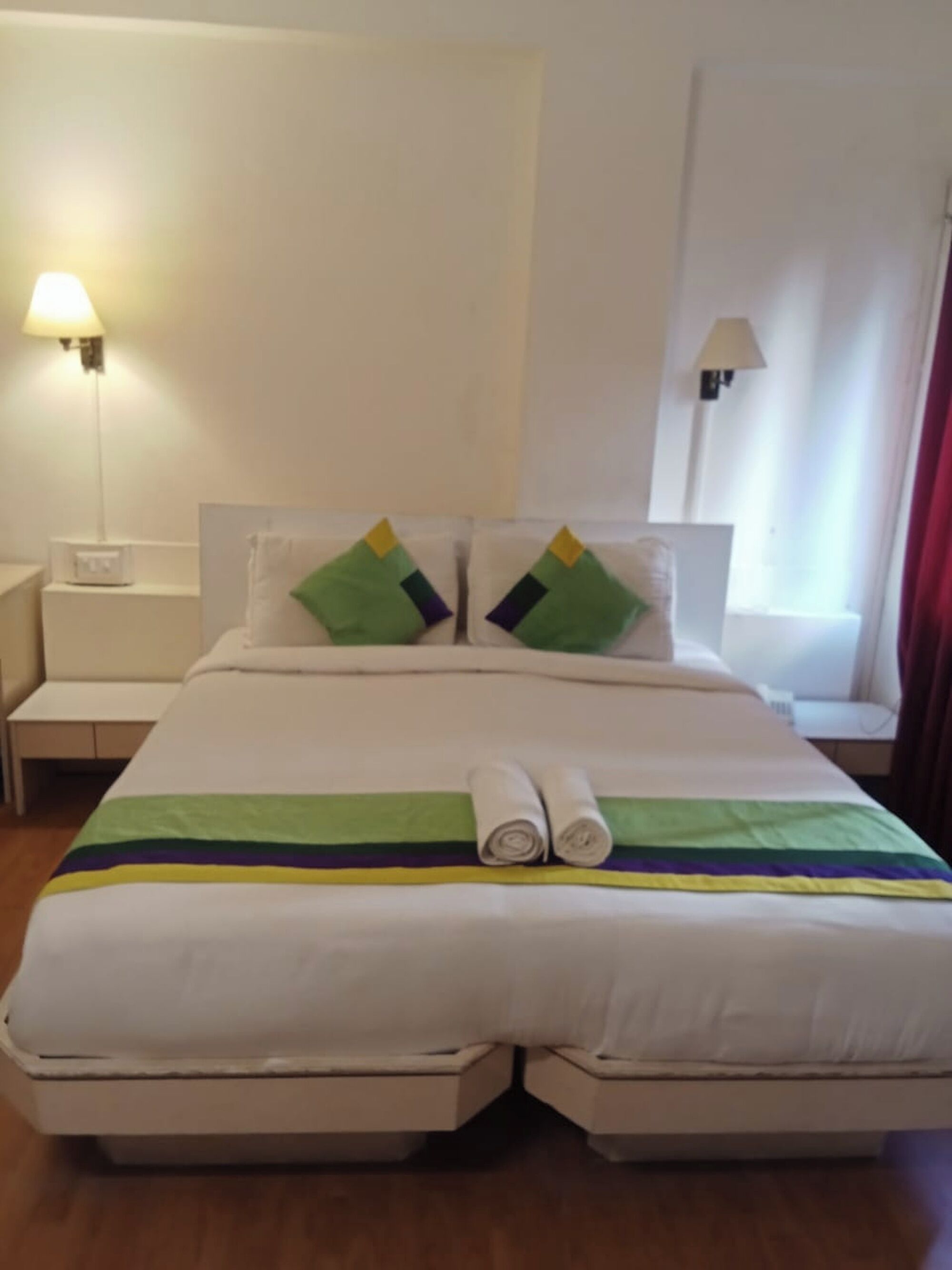A double bed with a white and green striped bedspread, two pillows with green and yellow accents, and two rolled towels on the bed.