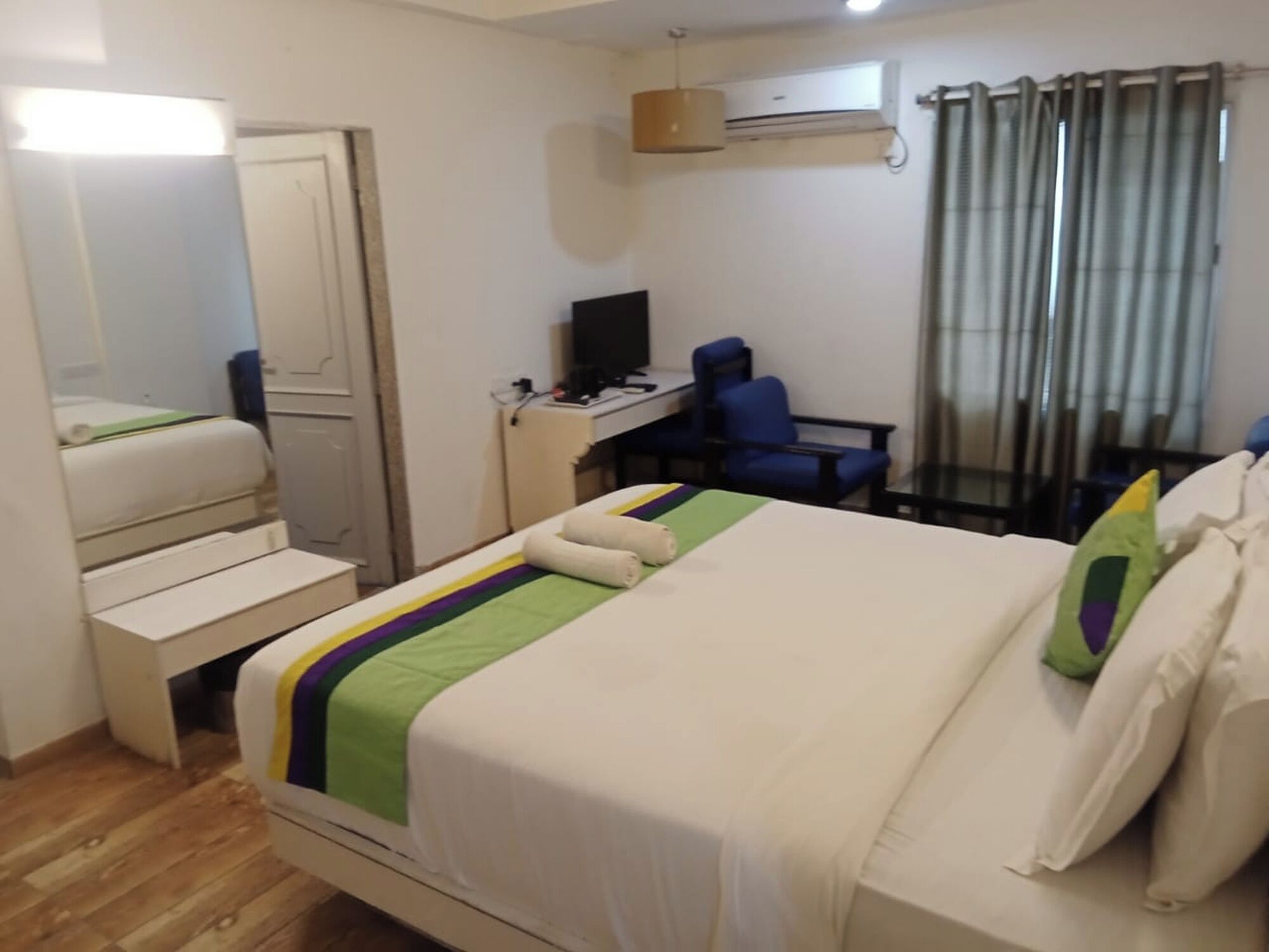 A hotel room with a bed, a desk, a chair, an air conditioner, and a window with curtains.