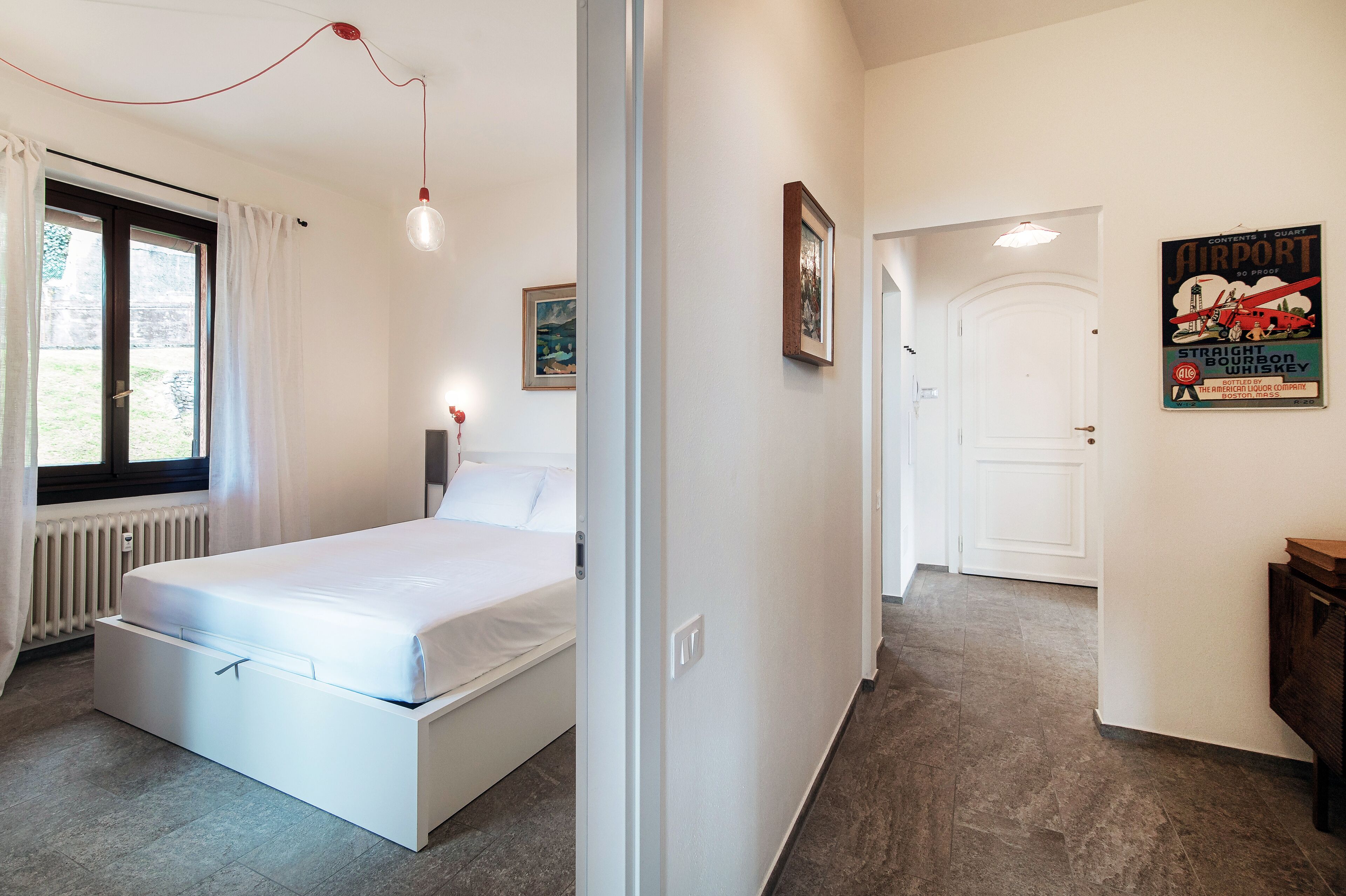 Une chambre à coucher comprenant un lit, un radiateur, une fenêtre avec des rideaux et une porte donnant sur une autre pièce.