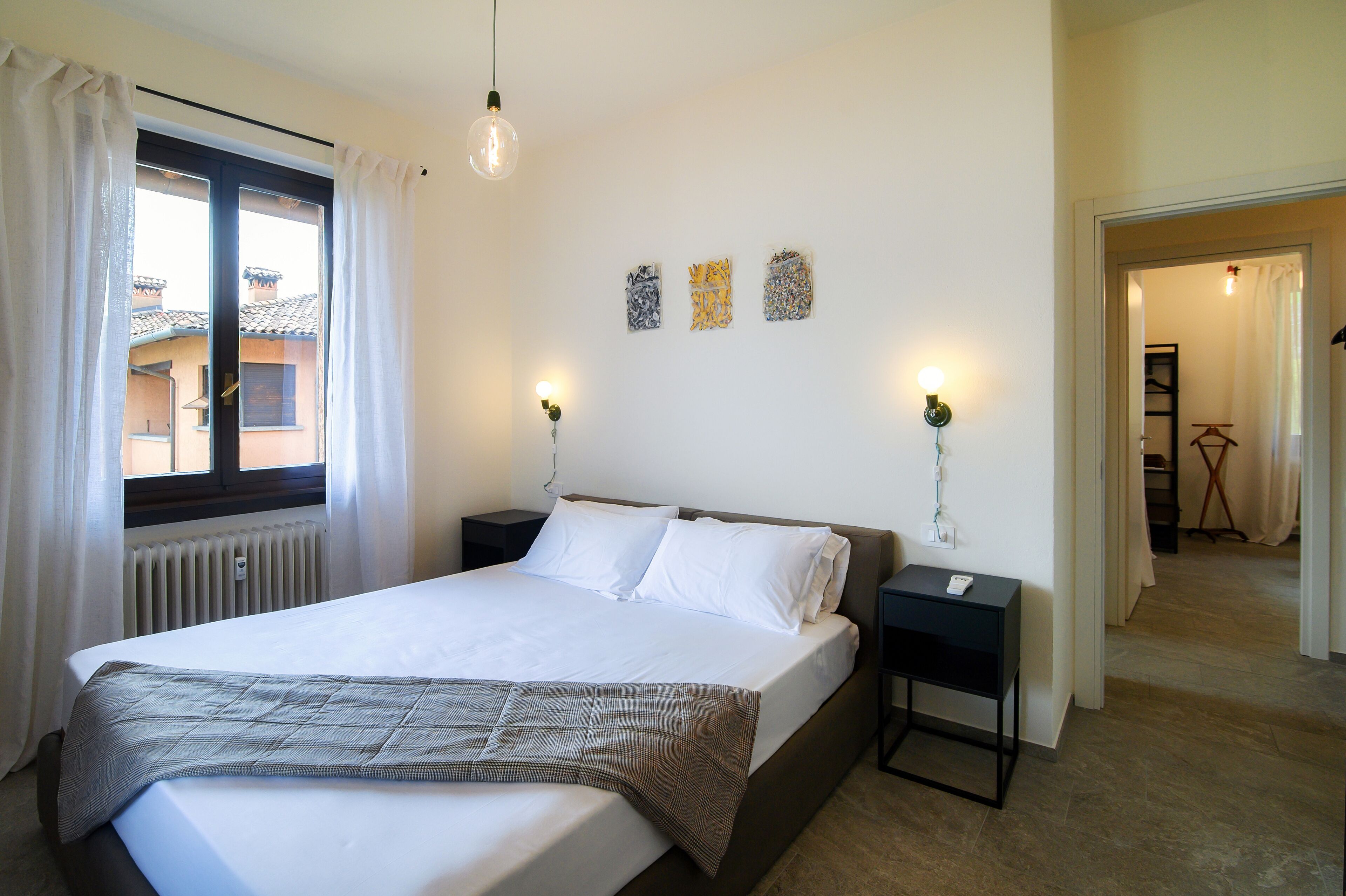 Een slaapkamer met een groot bed, twee nachtkastjes, een raam met gordijnen en drie wandlampen.