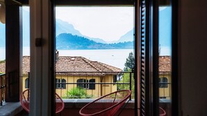 Ein Balkon mit Blick auf einen See, Berge und ein gelbes Gebäude mit einem Ziegeldach.